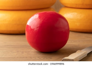 Whole Dutch Red Edam Cheese On A Cutting Board And Large Cheeses At The Background