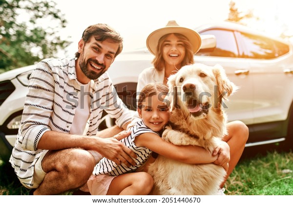 The whole family came to nature for the
weekend. Mom and Dad with their daughter and a Labrador dog are
standing near the car. Leisure, travel,
tourism.
