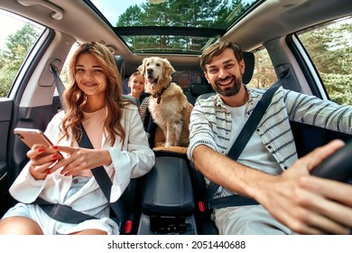 The Whole Family Is Driving For The Weekend. Mom And Dad With Their Daughter And A Labrador Dog Are Sitting In The Car. Leisure, Travel, Tourism.
