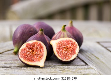 Whole figs and one fig sliced in half on top of a teak garden table. Focus is on the sliced fig. - Shutterstock ID 318104699