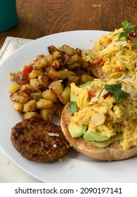 A Whole Food Plant Based Breakfast Or Brunch Of Semi-crisp Roasted Potato Hash Browns, A Plant-based Sausage Patty, And Plant-based Eggs On A Whole Wheat Bagel With Avocado. 