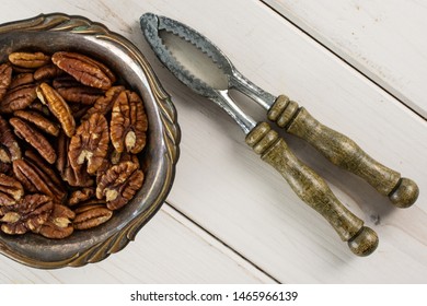 Lot Of Whole Fresh Brown Pecan Nut Half In Old Iron Bowl With Vintage Nutcracker Flatlay On White Wood