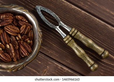 Lot Of Whole Fresh Brown Pecan Nut Half In Old Iron Bowl With Vintage Nutcracker Flatlay On Brown Wood