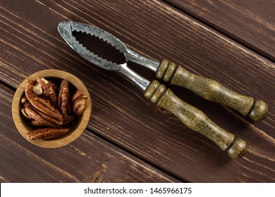 Lot Of Whole Fresh Brown Pecan Nut Half In A Wooden Bowl With Vintage Nutcracker Flatlay On Brown Wood