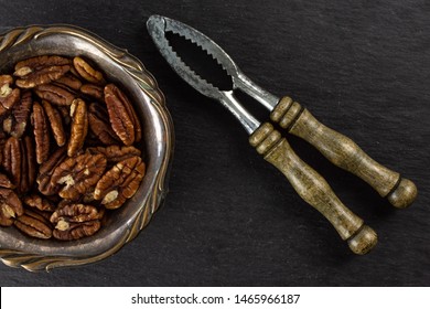 Lot Of Whole Fresh Brown Pecan Nut Half In Old Iron Bowl With Vintage Nutcracker Flatlay On Grey Stone