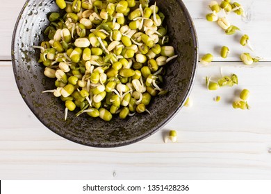 Lot of whole fresh green bean sprouts mungo in a grey ceramic bowl flatlay on white wood
