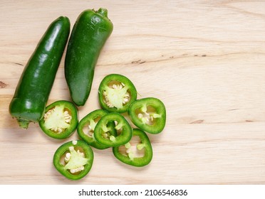 Whole fresh jalapeno peppers and slices on wooden board