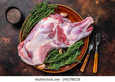 Whole fresh Raw goat shoulder meat on a plate. Dark wooden background. Top view.