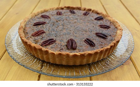 Whole freshly baked pecan pie on a glass plate, on a wooden table