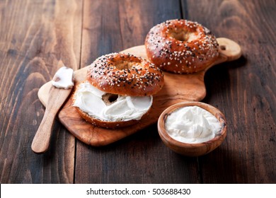Whole grain bagels with cream cheese on wooden board, selective focus