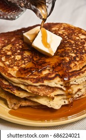 Whole Grain Flapjacks With A Pat Of Butter On Top And Warm Maple Syrup Being Poured On Top From A Crystal Glass Pitcher On A Round Yellow Plate