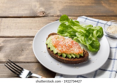 Whole grain rye bread toast with salmon and avocado on wooden table background. Healthy food, avocado open sandwich for breakfast or lunch