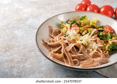 Whole grain tagliatelle pasta with vegetables like broccoli, tomatoes and spinach, served with parmesan in a plate on a gray background, copy space, selected focus, narrow depth of field - Powered by Shutterstock