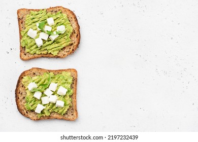 Whole grain toast with mashed avocado and white cheese cubes on grey concrete background. Top view with copy space.  - Powered by Shutterstock