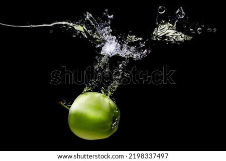 Whole green apple submerges underwater with splashes and bubbles on black background.