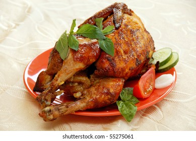 Whole Grilled Chicken Served On Red Plate Decorated With Vegetables And Mint