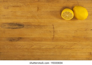 A whole and half lemon sit in the corner of a butcher block counter