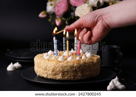 Whole holiday cake with crumbly shortcrust pastry and mini meringue. Man lights candles on a cake. Birthday cake with lit candles. Homemade baking. Black background, selective focus, close-up.