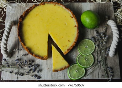 Whole Ideal Florida Key Lime Pie On The Wooden Tray With Rope Handles. Three Lime Slices, Lavender And Decorative Straw On The Instagram Layout.  Green, Vegetarian And Organic Flat Lay. 