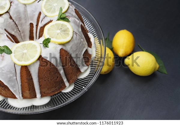 Whole lemon cream cheese bundt cake with slices of\
fresh lemons and mint on top. Extreme shallow depth of field with\
selective focus on cake.