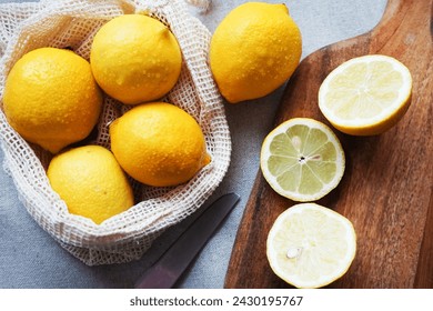 Whole lemons next to cut ones on a wooden board next to a knife on a light background - Powered by Shutterstock