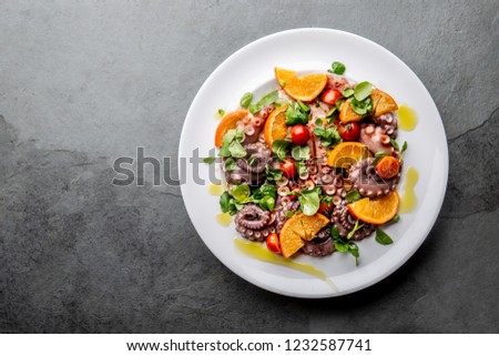Whole octopus salad with orange, tomatoes and cress salad on white plate. Top view.