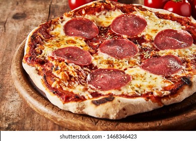 Whole oven-fired tasty Italian salami pizza with mozzarella and fresh herbs served on a wooden bard in a close up view for menu advertising