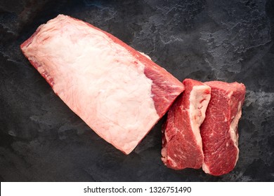 A whole piece of Beef Brisket with sliced two steaks on stone background, Top view