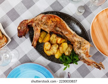 Whole piquant roasted rabbit with side dish of baked potato slices garnished with fresh herbs for dinner - Shutterstock ID 2230033837