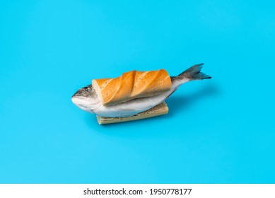 Whole Raw Fish Between Slices Of Bread On A Blue Colored Table. Eating Raw Fish Concept With A Frozen Dorado Fish In A Sandwich