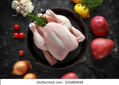 Whole raw Free range chicken in rustic skillet with rosemary leaf, thyme, lemon, red potatoes and garlic. ready to cook - Shutterstock ID 1016804038