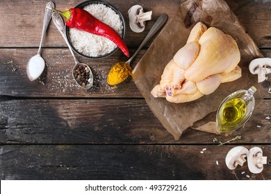 Whole Raw Mini Chicken On Baking Paper With Seasoning In Vintage Spoons, Sliced Mushrooms And Bowl Of Uncooked White Rice Over Old Wooden Background. Overhead View With Space For Text.