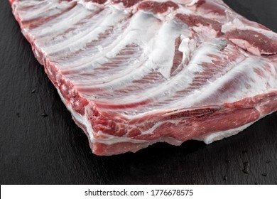 Whole raw pork ribs isolated on dark, black, stone board. spare ribs or belly. close-up Butchery, market, meat concept