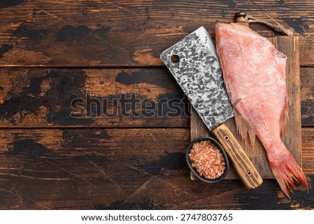 Whole raw redfish on rustic wooden board with butcher cleaver and sea salt. Fresh marine seafood ingredient for cooking