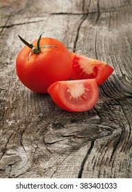 Whole red tomato with slice of tomato on wooden background closeup