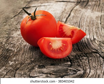 Whole red tomato with slice of tomato on wooden surface closeup