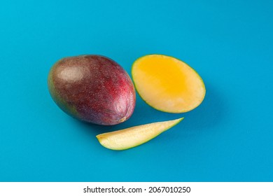 Whole, Ripe, Burgundy, Juicy And Very Tasty Mango Lies Together With A Cut In Half And A Separate Wedge. View From Above