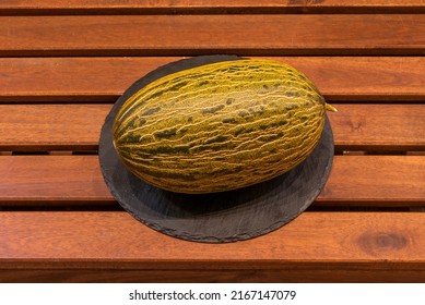 Whole ripe melon piel de sapo on round black slate plate