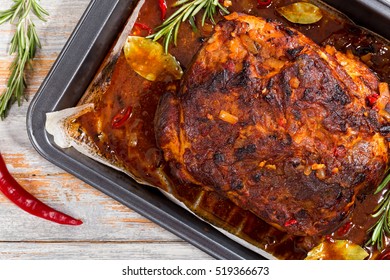 Whole Roast Shoulder Of Pulled Pork In Roasting Pan With Rich Spicy Hot Marinade On Old Wooden Table With Chili, Garlic And Rosemary. View From Above, Close-up