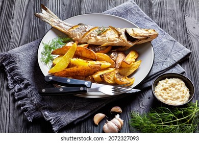 Whole Roasted Sea Bass Fish Served On A Plate With Sea Salt, Dill, French Fries Horseradish On A Black Wooden Table, Top View, Close-up