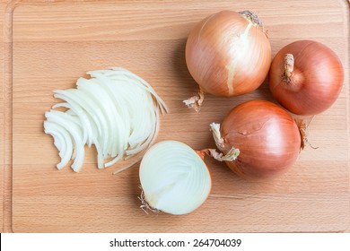 Whole and sliced onions on wooden cutting  board.