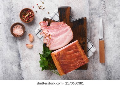 Whole Smoked Slab Bacon. Brisket. Sliced Smoked Gammon On A Wooden Table With Rosemary, Parsley, Pepper, Salt, And Garlic On Old Gray Concrete Table Background. Copy Space.