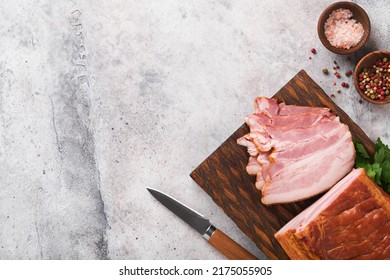 Whole Smoked Slab Bacon. Brisket. Sliced Smoked Gammon On A Wooden Table With Rosemary, Parsley, Pepper, Salt, And Garlic On Old Gray Concrete Table Background. Copy Space.