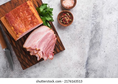 Whole Smoked Slab Bacon. Brisket. Sliced Smoked Gammon On A Wooden Table With Rosemary, Parsley, Pepper, Salt, And Garlic On Old Gray Concrete Table Background. Copy Space.