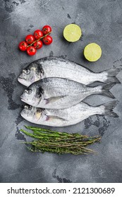 Whole Three  Seabream Or Gilt Head Bream Dorada Fish With Herbs Pepper Lime Tomato For Cooking And Grill On Grey Textured Background, Top View