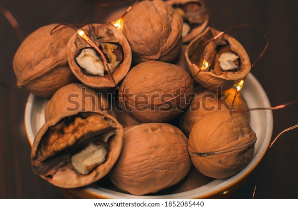 Whole walnuts and\
pecans, divided in half, lie in a ceramic bowl. Nuts close-up.\
Snack and Christmas\
lights