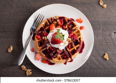 Whole wheat Belgium waffle topped with boysenberry syrup, whipped cream, walnuts, and freshly chopped strawberries top view