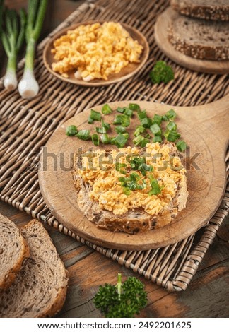 Whole wheat bread with appetizing eggs salad, decorated with fresh chives on wooden board