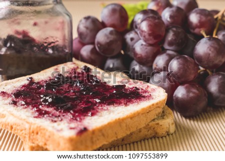 Whole wheat bread with grape jelly spread on wooden table.