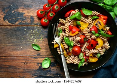 Whole Wheat Fusilli Pasta With Grilled Vegetables In A Black Bowl On A Wooden Background. Top View With Copy Space.